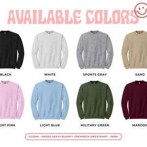 May include: A display of crewneck sweatshirts in various colors: black, white, sports gray, sand, light pink, light blue, military green, and maroon. The text "AVAILABLE COLORS" is at the top. The brand is Gildan.