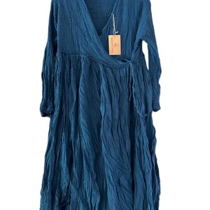 May include: A long-sleeved, deep blue wrap dress with a V-neckline and a textured, crinkled fabric finish. The dress features a side tie closure at the waist and a flowing, loose-fitting skirt. A small rectangular brown paper tag is attached.