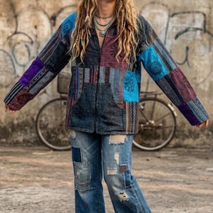 May include: A long-sleeve zip-up jacket featuring a patchwork design in shades of blue, purple, and black with various patterns, paired with distressed blue denim jeans that have frayed hems and multiple patches throughout the fabric.