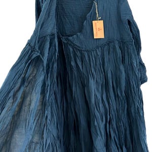 May include: A dark blue long-sleeved dress made of crinkled fabric with a wrap-style front, a gathered waistline, and a V-neckline. A small rectangular tan paper tag is attached to the neckline with string, featuring printed text and a logo.