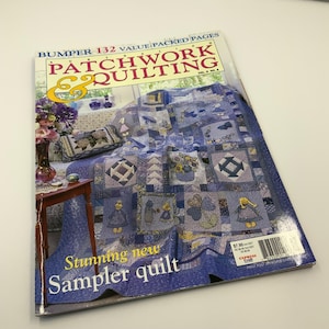 May include: A magazine titled "Patchwork & Quilting" with a blue and white quilt on the cover. The cover also features text that reads "Stunning new Sampler quilt". The magazine is open on a white surface.