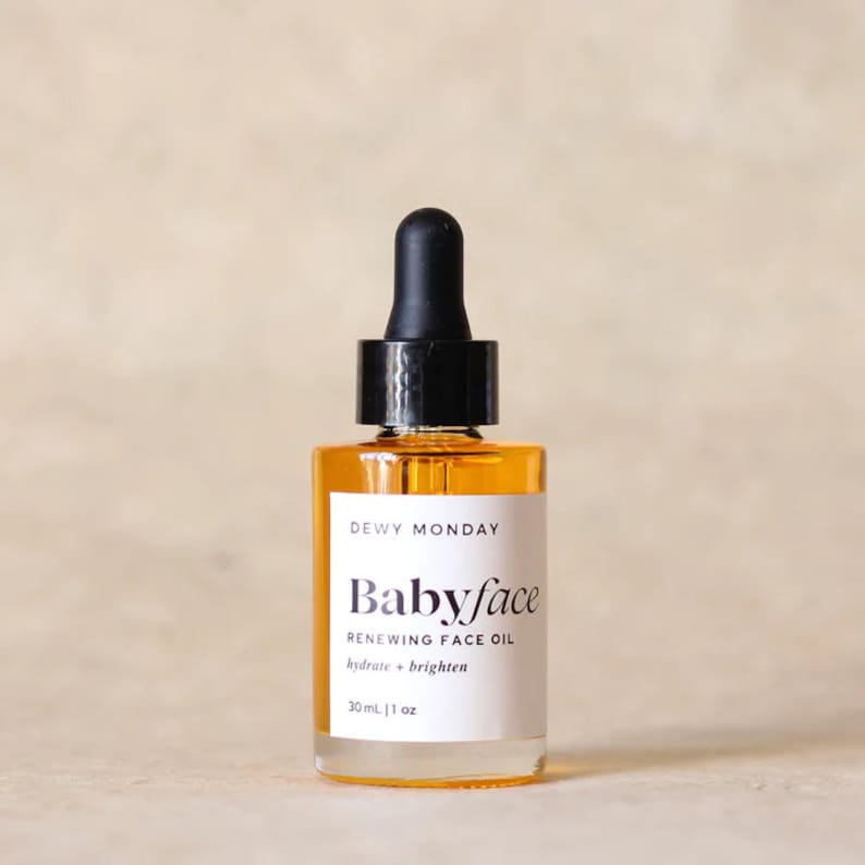K&ouml;nnte beinhalten: Eine durchsichtige Glasflasche mit einem schwarzen Tropfer oben, gef&uuml;llt mit einer gelben Fl&uuml;ssigkeit. Das Flaschenetikett lautet "DEWY MONDAY Babyface RENEWING FACE OIL hydrate + brighten 30mL | 1 oz"