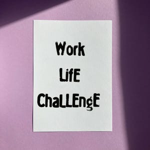 Könnte beinhalten: Eine weiße rechteckige Karte mit den Worten "Work Life Challenge" in fetter, schwarzer, handschriftlicher Schrift. Die Karte befindet sich vor einem hellvioletten Hintergrund mit einem Schatten.