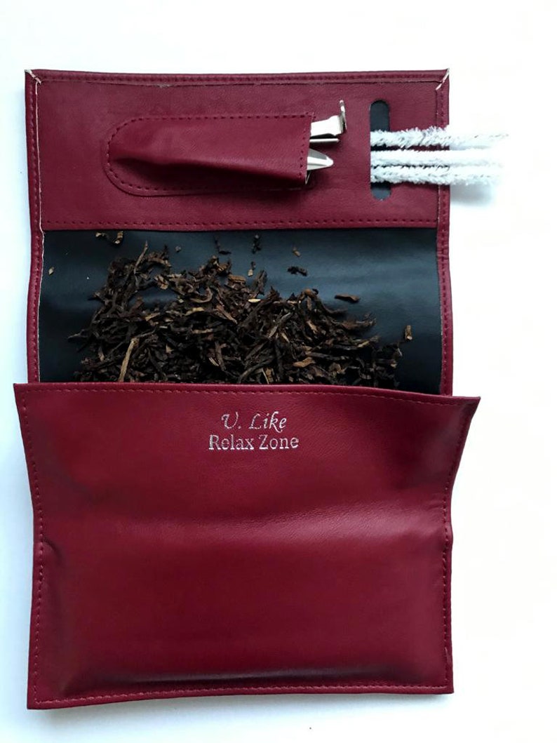 Puede incluir: Una bolsa de tabaco de cuero rojo con forro negro. La bolsa tiene un bolsillo para una herramienta y una ranura para un limpiador de pipa. La bolsa est&aacute; abierta y hay tabaco dentro. La bolsa tiene el texto "U. Like Relax Zone" impreso en la parte delantera.