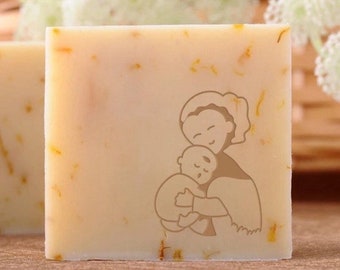 May include: A bar of soap with a design of a mother holding a child. The soap is white with flecks of yellow.
