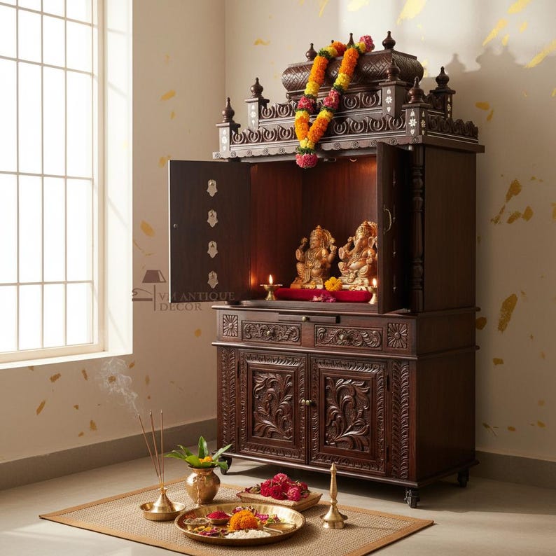 K&ouml;nnte beinhalten: Ein dunkelbrauner Holztempelschrank mit kunstvollen Schnitzereien und offenen T&uuml;ren. Im Inneren sitzen goldene Statuen auf einem roten Tuch, beleuchtet von Kerzen. Eine Blumengirlande h&auml;ngt von oben. Weihrauch und Opfergaben sind davor angeordnet.