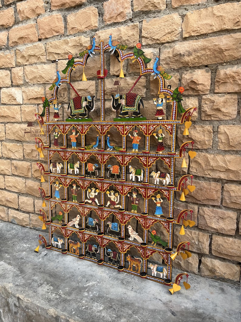 Puede incluir: Un adorno de pared rectangular de metal con varios niveles, que presenta un marco rojo con patrones florales blancos. Contiene numerosos estantes peque&ntilde;os que exhiben figuras pintadas de animales, aves y personas, con dijes amarillos.