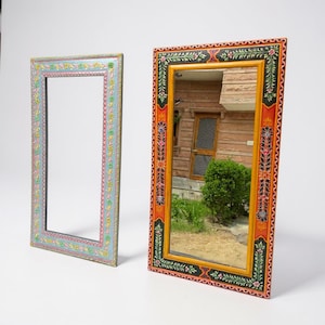 Puede incluir: Dos espejos de pared rectangulares con marcos pintados a mano. Un marco es azul claro con patrones florales multicolores. El segundo marco es naranja con bordes negros e intrincados diseños de enredaderas florales verdes, rojas y blancas.