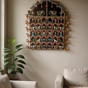 Puede incluir: Un gran adorno de pared arqueado con una estructura de madera de varios niveles sobre un fondo negro. Muestra numerosas figuras pintadas a mano de animales y personas en compartimentos individuales, acentuadas por peque&ntilde;as campanas amarillas.
