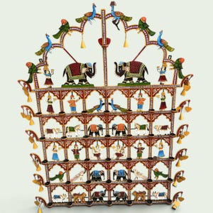 Puede incluir: Un adorno de pared de metal de varios niveles con detalles pintados a mano de elefantes, tigres, vacas, pavos reales y figuras humanas. La estructura est&aacute; decorada con peque&ntilde;as campanas colgantes y arcos ornamentados en tonos rojo, azul y oro.
