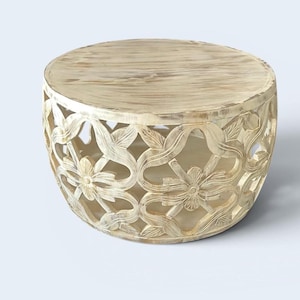 Könnte beinhalten: Ein runder Couchtisch aus Holz mit einer hellbeigen, gekalkten Oberfläche. Der Sockel weist ein kompliziertes, durchbrochenes Schnitzdesign auf, das aus sich wiederholenden Blumenmotiven und fließenden, miteinander verbundenen Rankenmustern besteht.