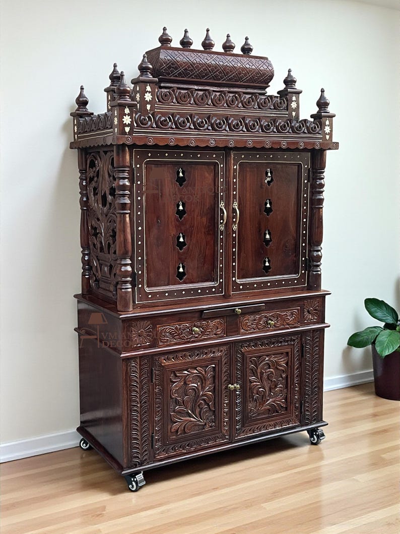 K&ouml;nnte beinhalten: Ein dunkelbrauner Holzschrank mit aufwendigen Schnitzereien und Intarsien. Der Schrank hat mehrere T&uuml;ren, Schubladen und dekorative Zierelemente. Er steht auf Rollen und hat ein traditionelles Design.