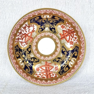 Könnte beinhalten: Ein dekorativer, runder Keramikteller mit einem zentralen Loch. Der Teller hat einen goldenen Rand und komplizierte Muster in Marineblau, Orange und Weiß. Florale und geometrische Designs zieren die Oberfläche und schaffen eine Vintage-Ästhetik.