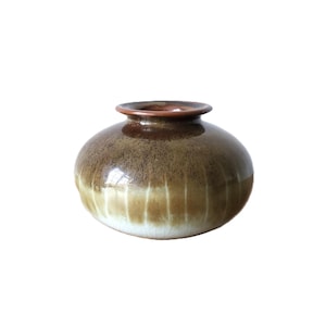 May include: A small, round ceramic vase with a brown and tan speckled glaze. The vase has a narrow opening and a rounded body, with vertical lines. The rim is a darker brown colour.