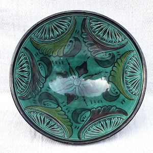 May include: A round ceramic bowl featuring a vibrant emerald green glaze with dark brown accents. The interior surface is decorated with four symmetrical, fan-shaped relief patterns and a central floral motif, all finished with a glossy sheen.