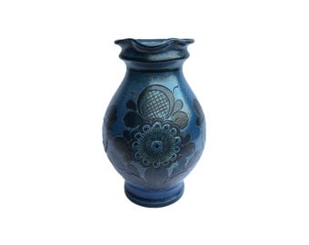 May include: A blue ceramic vase with a floral design. The vase has a wide mouth and a rounded body. The floral design is in black and white and features a large flower in the center.