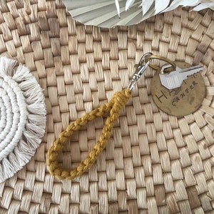 May include: A mustard yellow braided keychain with a silver key ring and a brass tag that says "Happy Camper".
