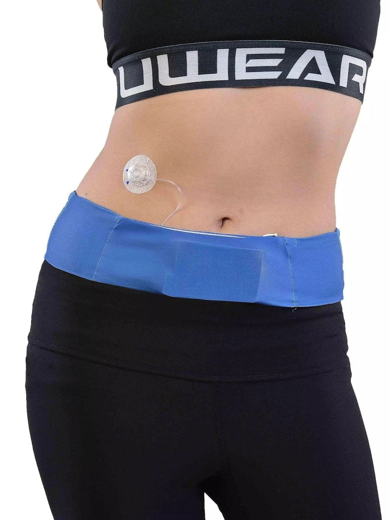 May include: A blue waist belt with a hook and loop closure is worn over black athletic pants. A medical device is attached to the abdomen. The top is a black sports bra with the word "UWEAR" printed in white.