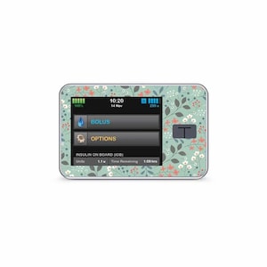 Peut inclure: Un appareil médical vert clair avec un motif floral. L'écran affiche l'heure, la date et les niveaux d'insuline. L'appareil possède des boutons pour "Bolus" et "Options".