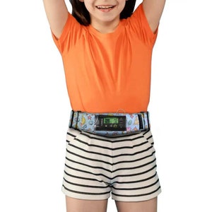 Puede incluir: Una persona joven que lleva una camiseta naranja brillante y pantalones cortos de rayas blancas y negras. Lleva un cinturón estampado en azul y blanco con un pequeño dispositivo negro sujeto a él. El dispositivo tiene una pantalla digital y botones.