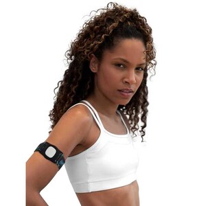 Può includere: Una donna indossa un reggiseno sportivo bianco e un braccialetto nero con un design blu e bianco.