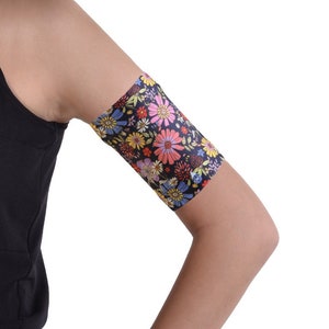 Puede incluir: Una manga de brazo negra con un estampado floral colorido. La manga está hecha de un material suave y elástico, ideal para proteger la piel del sol.