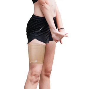 Può includere: Una fascia per coscia beige con un logo bianco. La fascia è indossata sulla coscia sinistra di una persona che indossa pantaloncini sportivi neri.