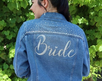 Pode incluir: Uma jaqueta jeans azul com um design de strass branco que diz "Bride" nas costas.