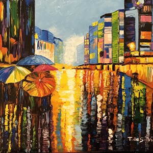 May include: A colorful oil painting of a city street scene with people walking under umbrellas in the rain. The buildings are brightly colored and the street is reflecting the light of the sky. The artist's signature, "T.deSilvia", is in the lower right corner.