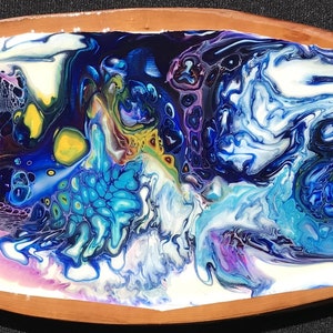 Könnte beinhalten: Eine ovale Holzschale mit einem farbenfrohen abstrakten Gemälde. Das Gemälde zeigt wirbelnde Blau-, Lila- und Weißtöne mit einem Hauch von Gelb und Grün. Der Rand der Schale ist aus Naturholz.