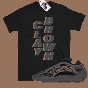 May include: Black t-shirt with the word "CBRAWYN" in layered gray and brown text. A gray and brown sneaker is positioned below the shirt. A white tag with a shoe graphic hangs from the shirt.