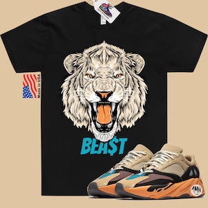 May include: Black t-shirt featuring a detailed illustration of a roaring white lion's head with the word "BEAST" in blue. Paired with tan, brown, and orange sneakers. Includes a "Made in USA" tag and a shoe tag.