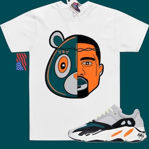 May include: White t-shirt with a graphic of a teal bear head with a barbed wire crown and Kanye West's face on the right side. The graphic says "YZY". A pair of grey, black, and orange Yeezy 700 sneakers are shown below the t-shirt.