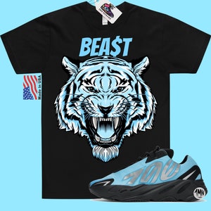 以下が含まれることがあります： 青い虎のグラフィックと青い「BEAST」の文字が書かれた黒いTシャツ。側面に「700」の数字が書かれた青と黒のスニーカーのペア。