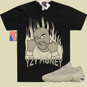 May include: Black t-shirt with a graphic of a masked figure with flames behind them. The text "YZY MONEY" is printed below the figure. A pair of beige sneakers are also pictured.