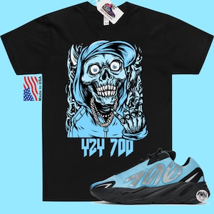 May include: Black t-shirt with a blue and white illustration of a skull wearing a hoodie and a chain. The text "424 700" is printed below the illustration. A pair of blue and black sneakers with the text "700" on the side are also shown.