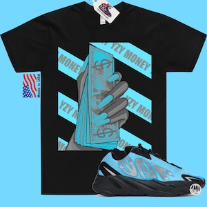 May include: Black t-shirt with a graphic of a hand holding a stack of blue bills with the text "YZY MONEY" on it.  A pair of black and blue sneakers with the text "YZY" on the side are in the bottom right corner of the image.