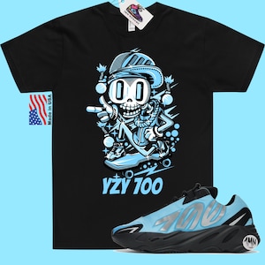 May include: Black t-shirt with a cartoon skeleton skateboarding graphic and the text "YZY 700".  A pair of light blue and black Yeezy 700 sneakers are also pictured.