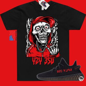 May include: Black t-shirt with a red skull wearing a red hoodie and making a middle finger gesture. The text "424 350" is printed below the skull. A pair of black and red Yeezy 350 Boost sneakers are shown below the t-shirt.