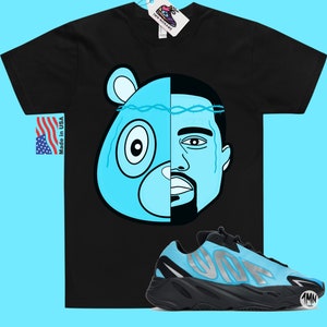 May include: Black t-shirt with a blue and black illustration of a bear and a man's face.  The t-shirt is paired with blue and black sneakers with the word "Yeezy" on the side.