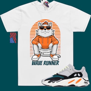 May include: White t-shirt with a cartoon cat wearing sunglasses and an orange hoodie. The cat is sitting on a striped background with the text "Wave Runner". A pair of grey, black, and orange sneakers are shown below the t-shirt.