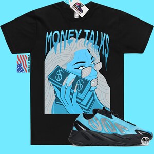 May include: Black t-shirt with a blue and white illustration of a woman holding a stack of money. The text "MONEY TALKS" is written in a dripping font above the woman. A pair of blue and black sneakers are shown below the illustration.