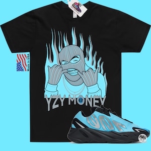 Puede incluir: Camiseta negra con una ilustraci&oacute;n azul y gris de una persona con pasamonta&ntilde;as y el texto "YZY MONEY". Un par de zapatillas azules y negras con el texto "YZY" en el lateral.