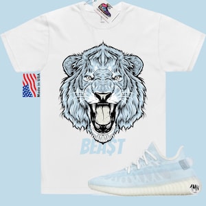Peut inclure: T-shirt blanc avec un motif de lion bleu et le mot "BEAST" imprim&eacute; en dessous. Le t-shirt est associ&eacute; &agrave; des baskets bleu clair et blanches.