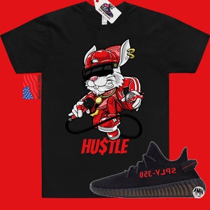 May include: Black t-shirt with a cartoon rabbit wearing a red hat, sunglasses, and a gold chain. The rabbit is holding a microphone and a spray can. The text "HUSTLE" is printed below the rabbit. A pair of black and red sneakers with the text "YZY-350" are shown below the t-shirt.
