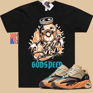 May include: Black t-shirt with a cartoon illustration of a pill bottle skateboarding with the text "Godspeed". A pair of tan, orange, and blue sneakers with the text "1MN" on the side.