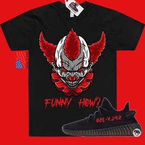 May include: Black t-shirt with a red and white clown face graphic and the text "FUNNY HOW?" in red. A black and red Yeezy 350 Boost sneaker is shown below the shirt.