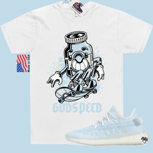 K&ouml;nnte beinhalten: Wei&szlig;es T-Shirt mit einer Cartoon-Illustration einer Pillenflasche, die Skateboard f&auml;hrt, mit dem Text "GODSPEED". Ein Paar hellblaue und wei&szlig;e Turnschuhe sind ebenfalls abgebildet.