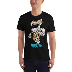 May include: Black t-shirt with a cartoon rabbit wearing a hat and holding a microphone. The rabbit is wearing a gold chain and has a backpack. The text "HUSTLE" is printed below the rabbit.