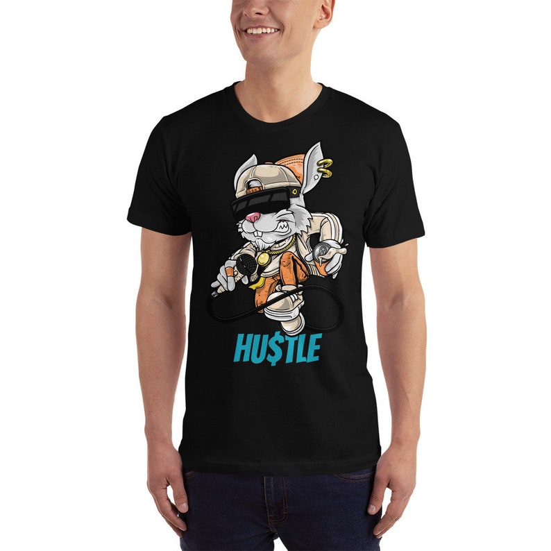 May include: Black t-shirt with a cartoon rabbit wearing a hat and holding a microphone. The rabbit is wearing a gold chain and has a backpack. The text "HUSTLE" is printed below the rabbit.